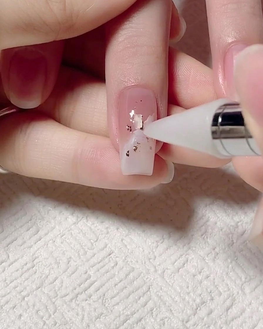 Ein Dotting-Tool platziert winzige, irisierende Muschelstücke auf dem Nagel.