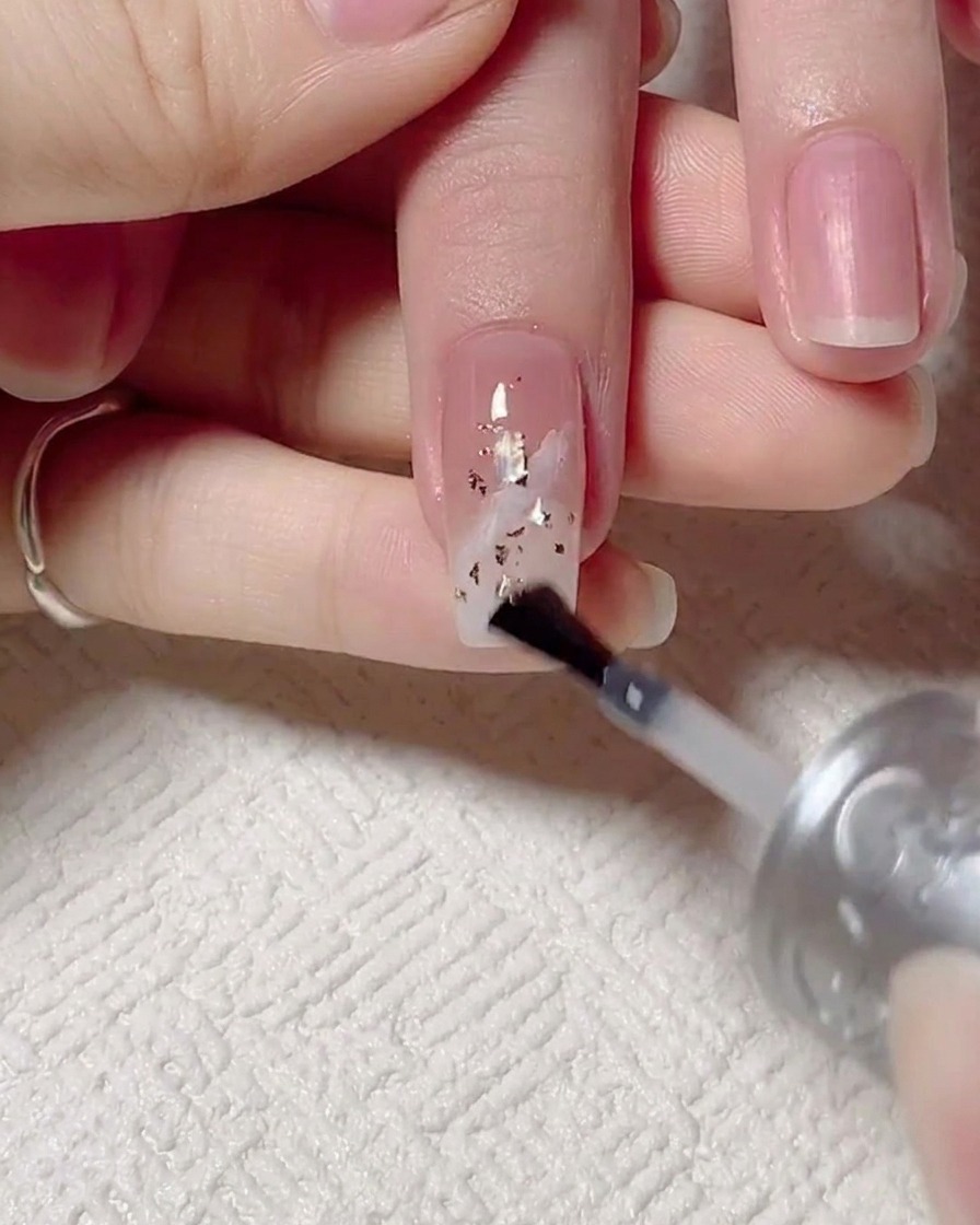 Ein Pinsel trägt einen glänzenden Top Coat auf, danach härtet der Nagel unter einer UV-Lampe aus.