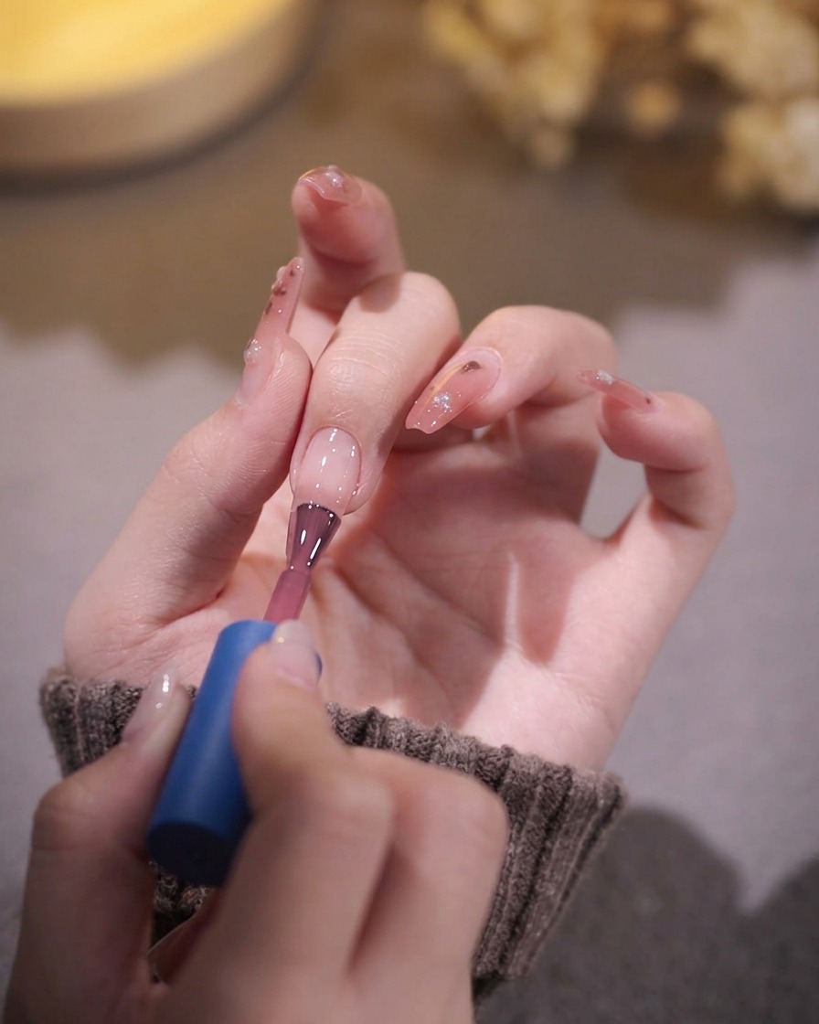 Ein Nagelpinsel trägt eine Schicht halbtransparentes rosa Gel auf einen vorbereiteten Nagel auf.