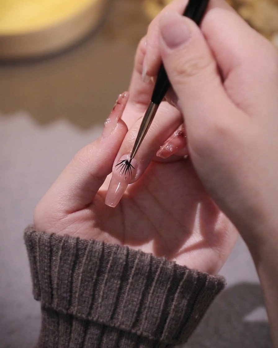 Ein feiner Liner-Pinsel korrigiert die Ränder des rosa Gels an einem Fingernagel.