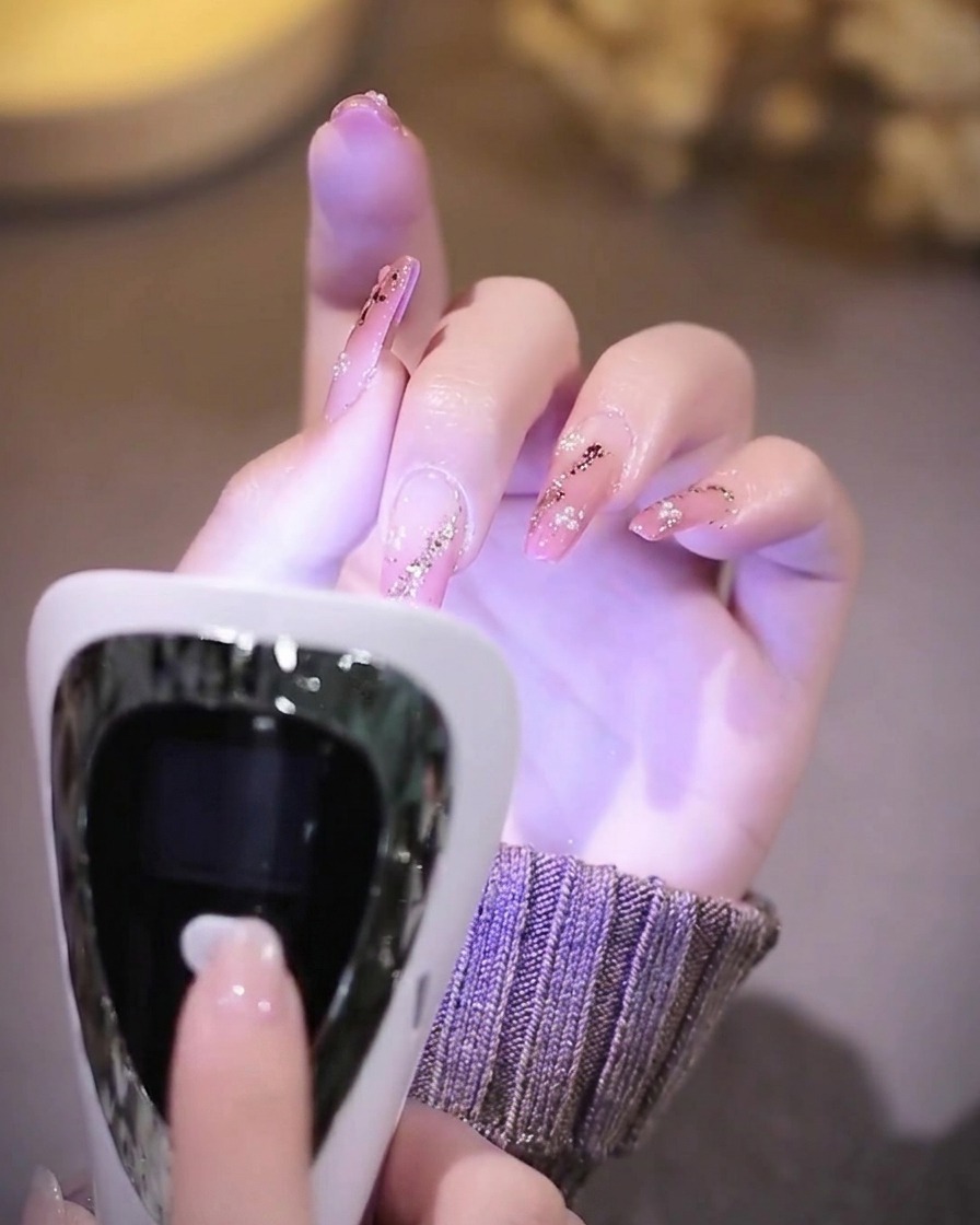 Eine Hand mit fertigen Nägeln in einer leuchtenden UV-Nagellampe.