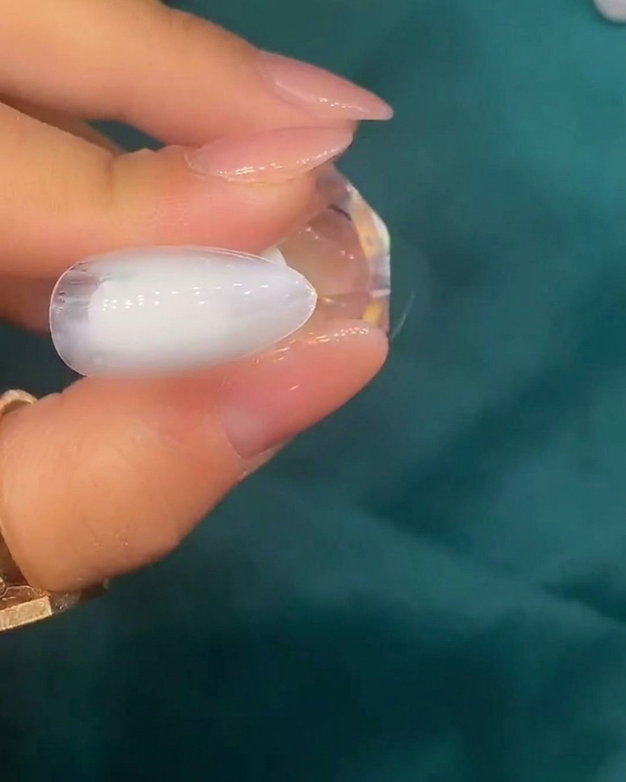 Eine Pinzette platziert kleine, irisierende Muschelstücke auf einer Nageloberfläche mit weißer Basis.
