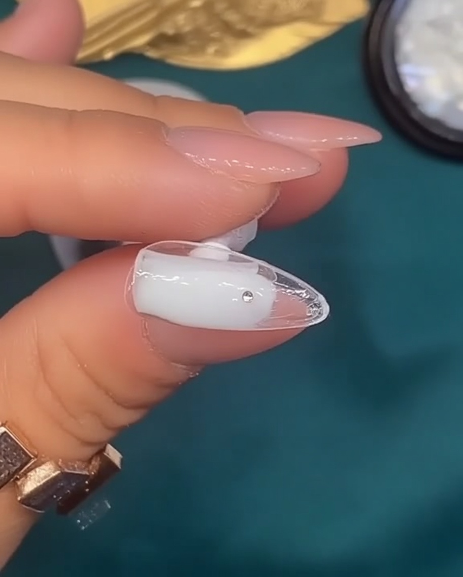 Ein Pinsel trägt ein durchscheinendes, milchig weißes Gel auf einen natürlich geformten Nagel auf.
