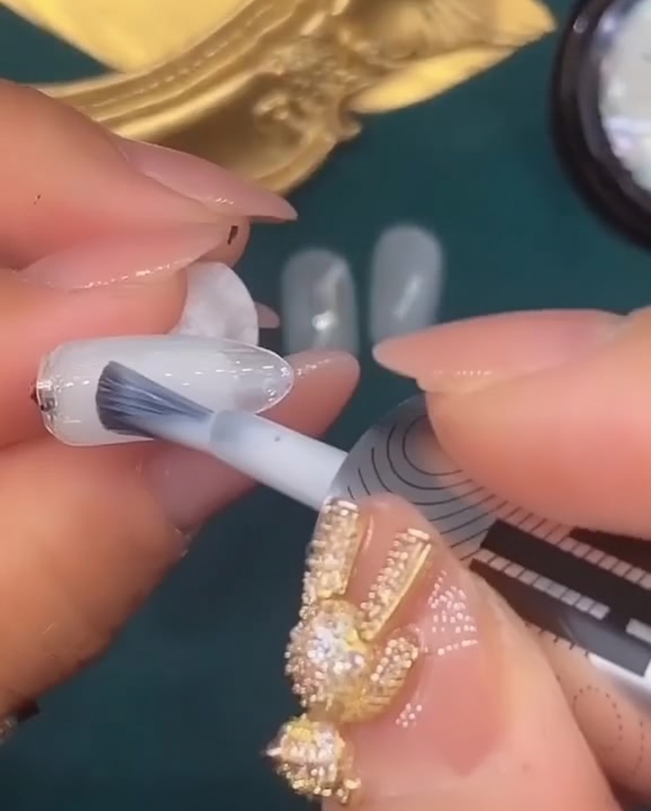 Ein Nagelpinsel trägt eine Schicht durchscheinendes weißes Gel auf den fünften Nagel auf.