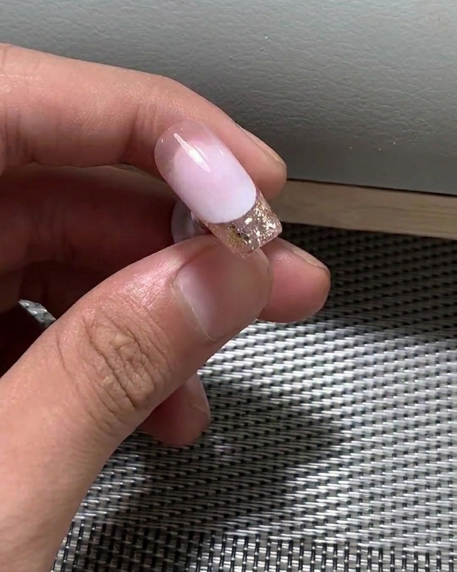 Nahaufnahme eines Pinsels, der eine dünne Schicht Nude-Gel-Nagellack auf einen Nagel aufträgt.
