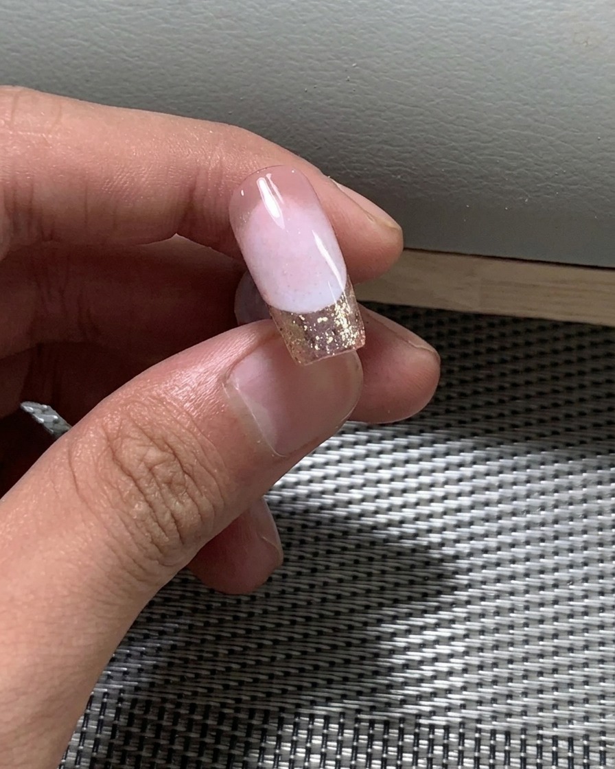 Nahaufnahme eines Pinsels, der eine zweite Schicht Nude-Gel-Nagellack auf einen Nagel aufträgt.