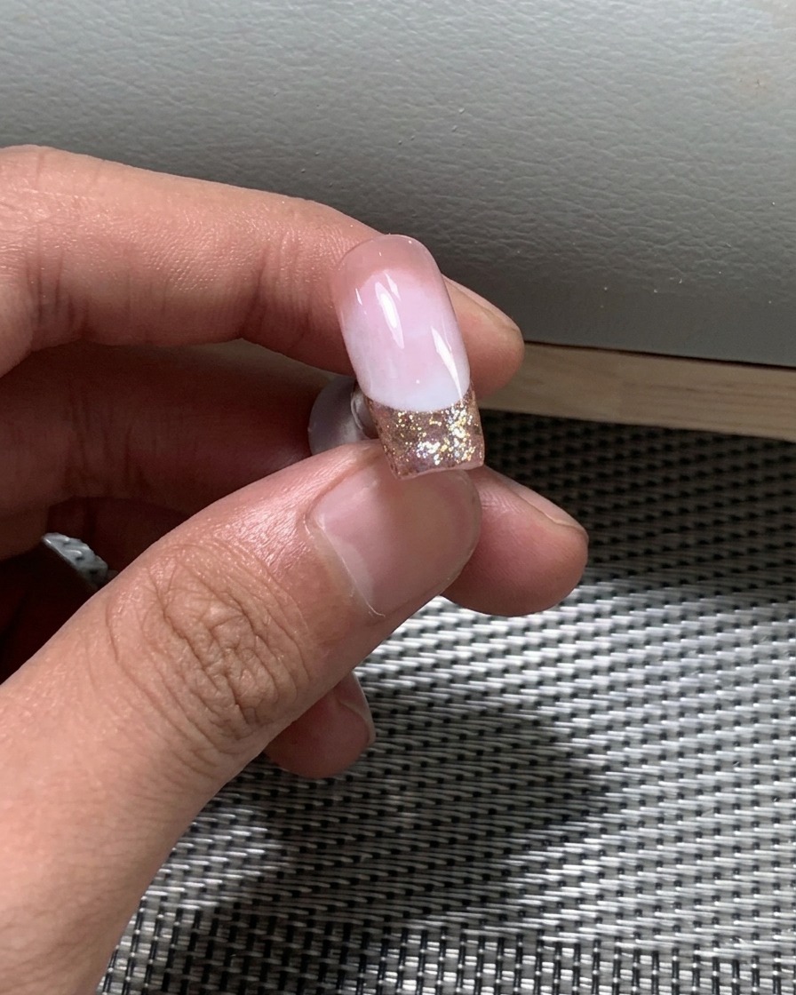 Nahaufnahme von feinem Glitzernagellack, der auf die freie Kante des Nagels aufgetragen wird.