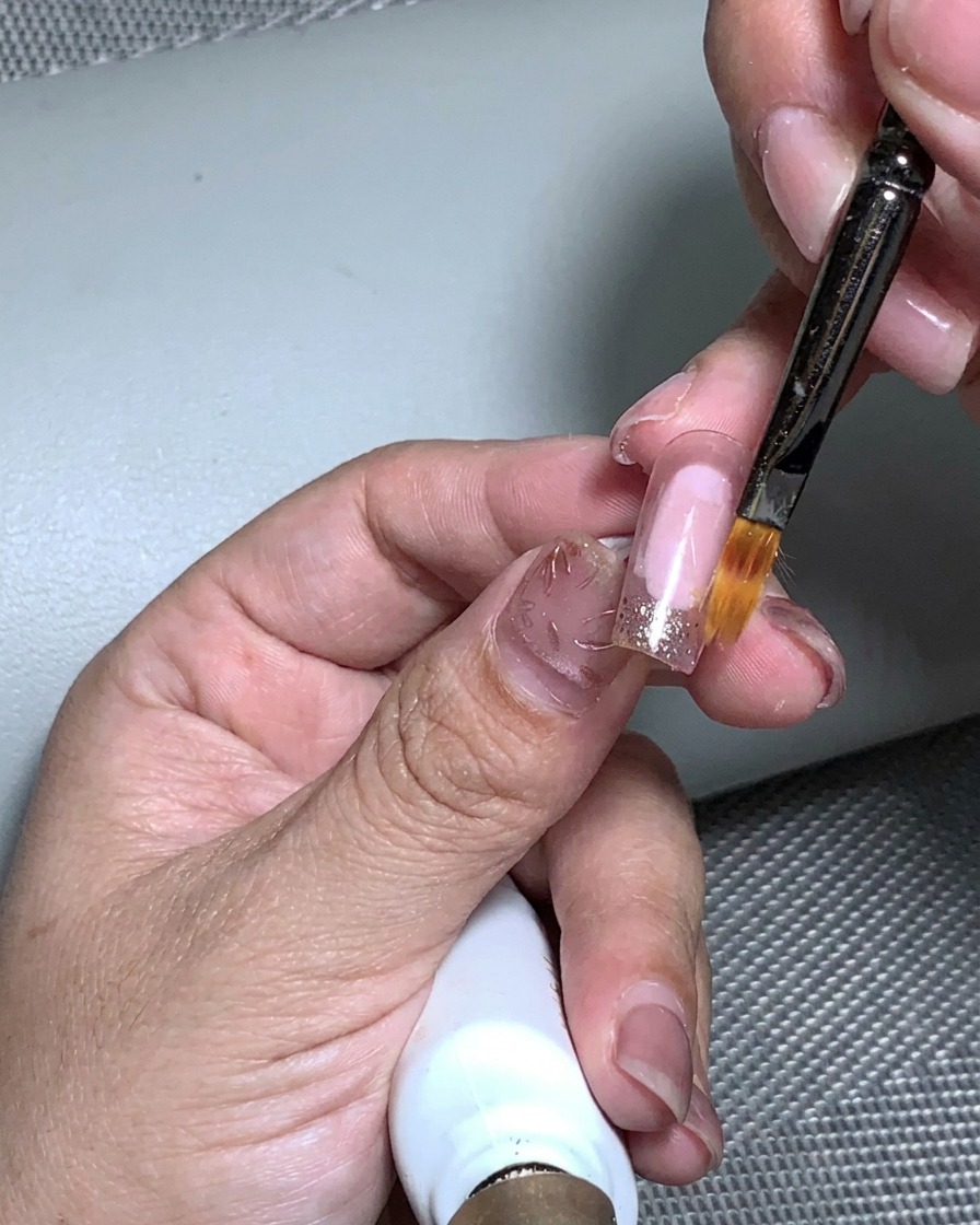 Eine Hand in einer UV-Nagellampe beim Aushärten des Blattgold-Auftrags.