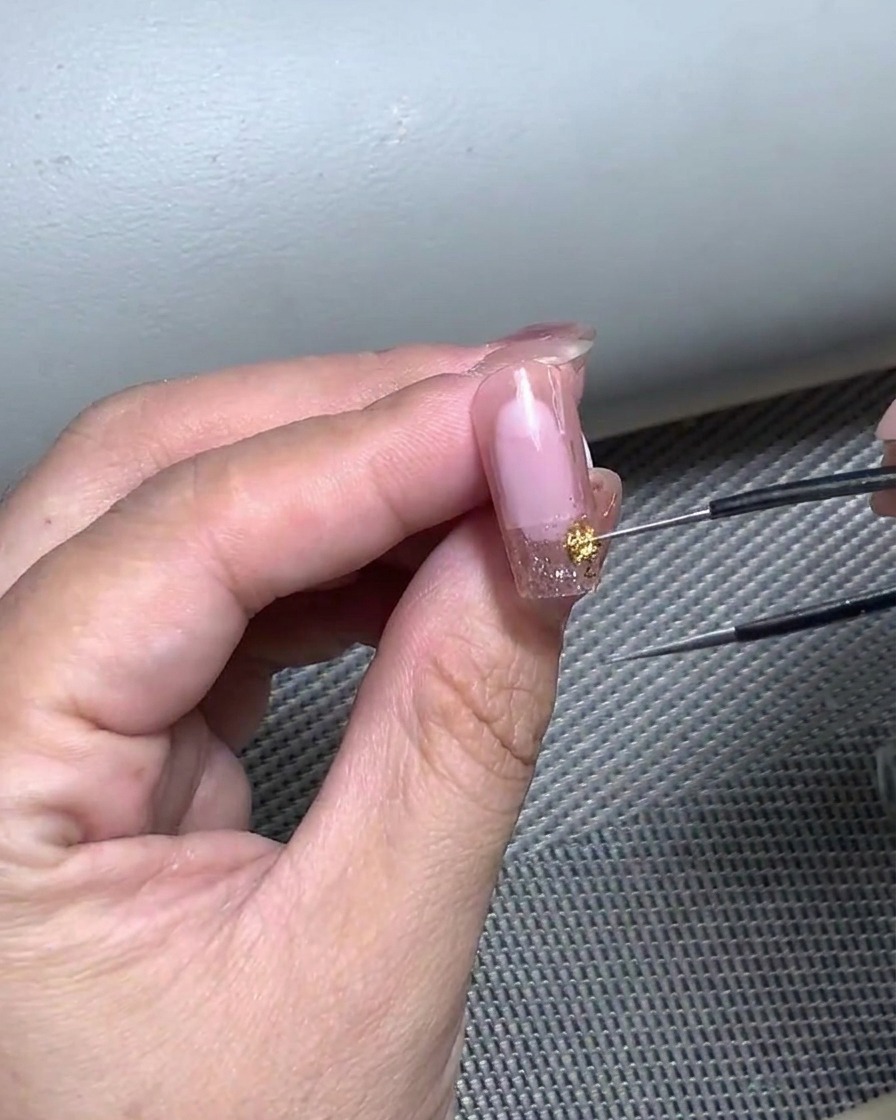 Nahaufnahme einer Hand, die mit einer Pinzette einen gebogenen French-Tip-Sticker auf einen für Gel vorbereiteten Nagel platziert.