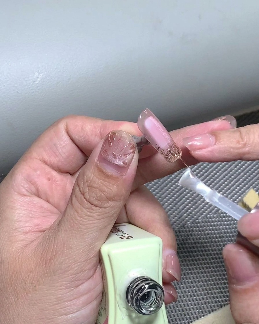 Ein Pinsel, der eine abschließende Schicht klaren Top Coat über ein vollendetes French-Tip-Nageldesign aufträgt.