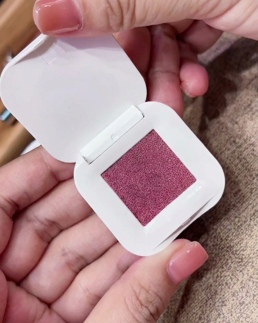 Ein dreieckiger Make-up-Schwamm drückt fest in ein quadratisches Kompaktpuder mit rosafarben-violettem Pigment.