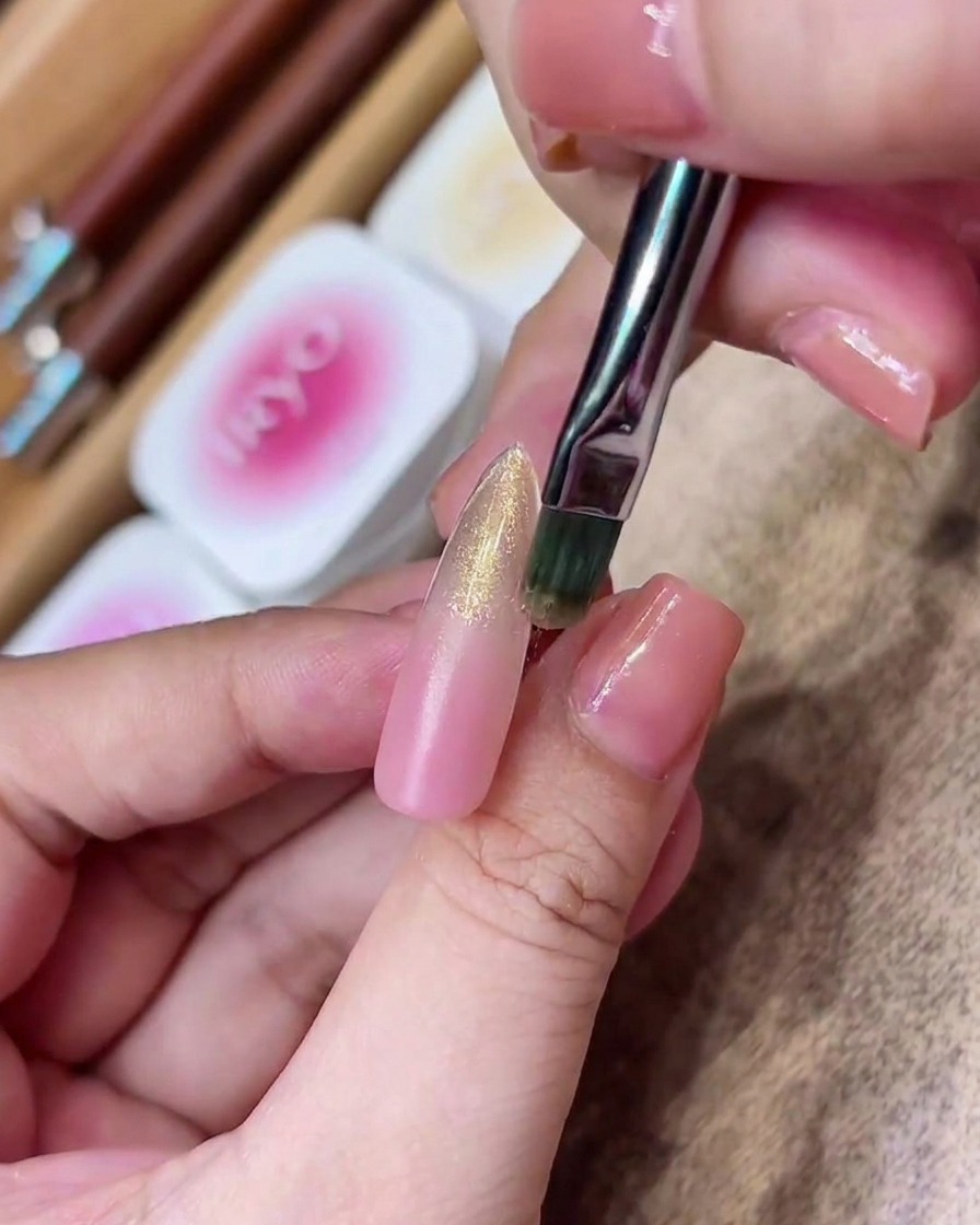 Ein Flachpinsel streicht ein transparentes, goldenes, magnetisches Gel auf den Bereich von der Mitte bis zur Spitze des Nagels.