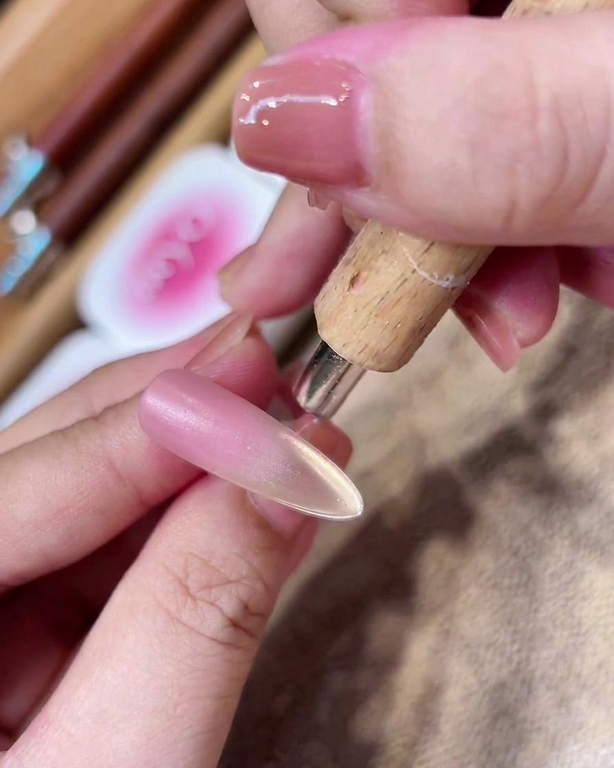 Ein zylindrischer Magnetstab wird nahe der Nagelspitze gehalten, um einen konzentrierten Streifen goldenen magnetischen Glitters zu erzeugen.