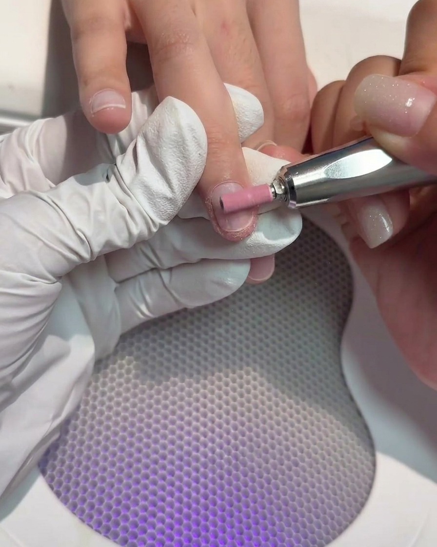 Ein zylindrischer Fräseraufsatz raut die Oberfläche eines Naturnagels an.