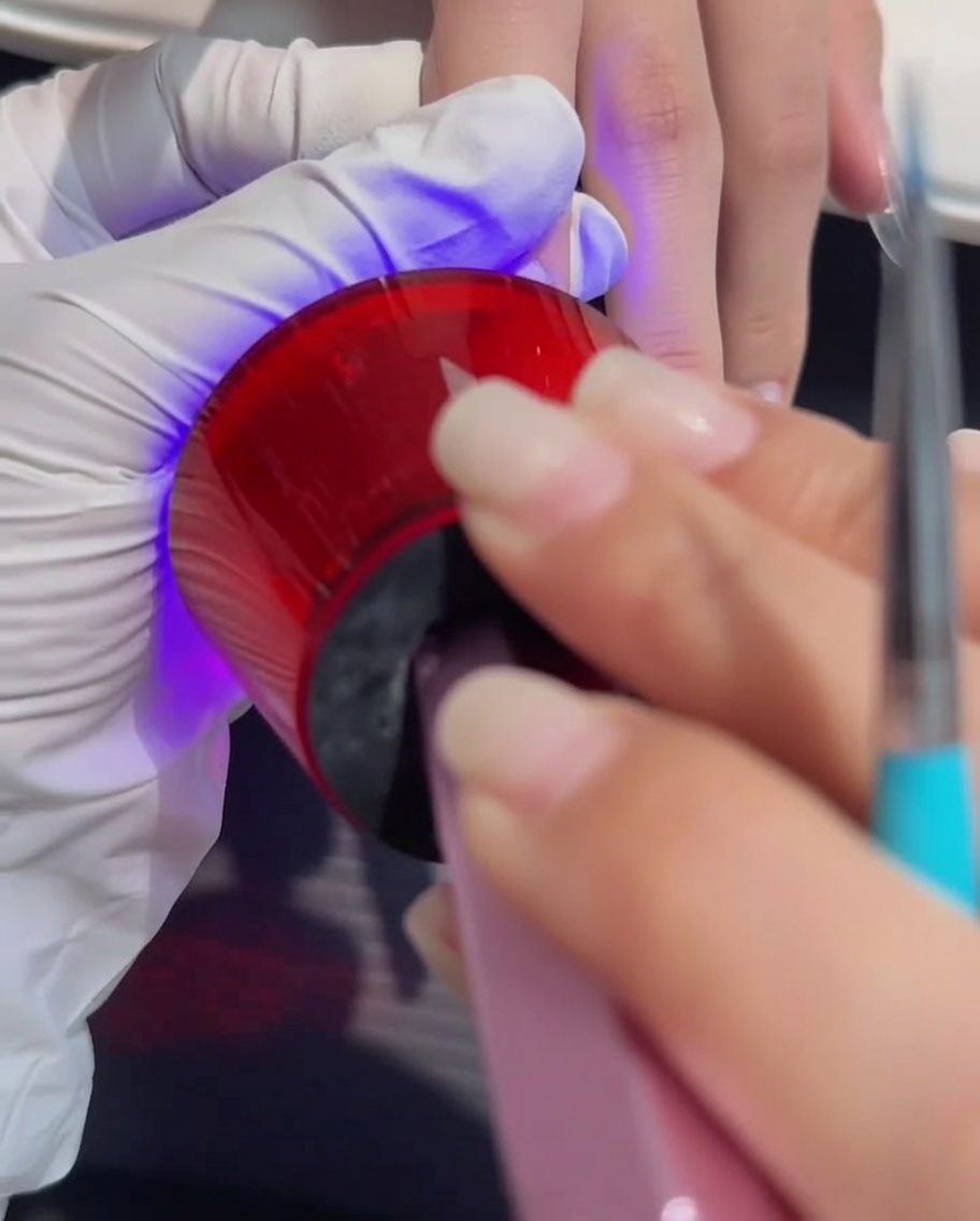 Eine Hand liegt während des Aushärtungsprozesses unter einer professionellen UV/LED-Lampe.