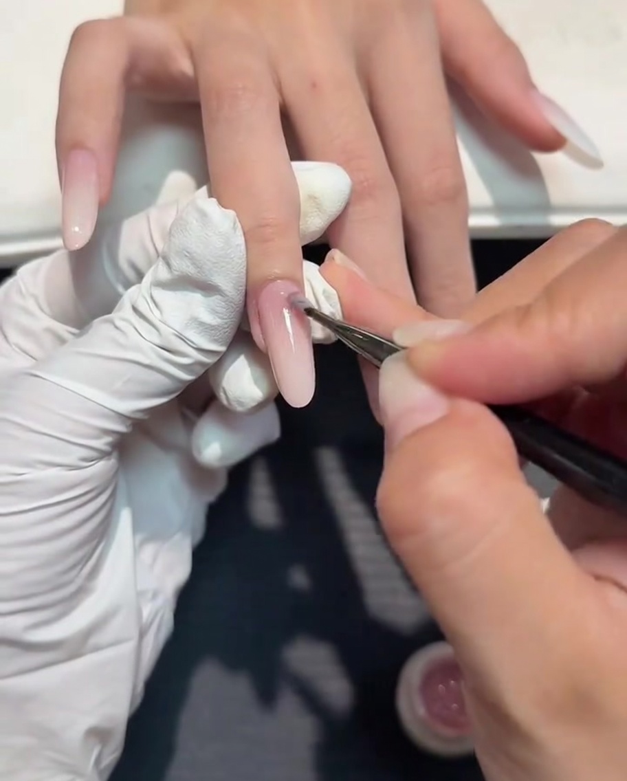 Ein kleiner Nail-Art-Pinsel trägt eine dünne Schicht Nude-Gel über dem weißen Ombré auf.