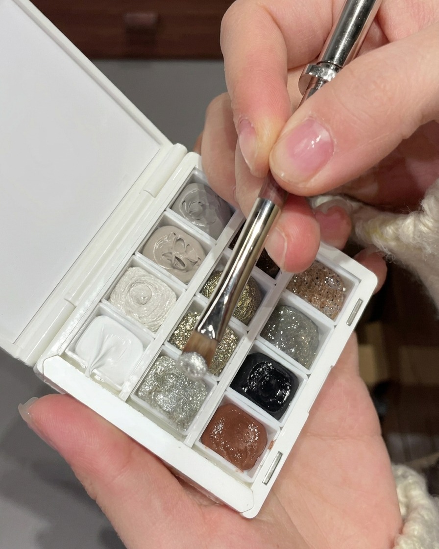 Ein Pinsel mischt feines silbernes Glitzergel mit größeren silbernen Pailletten auf einer weißen Nailart-Palette.