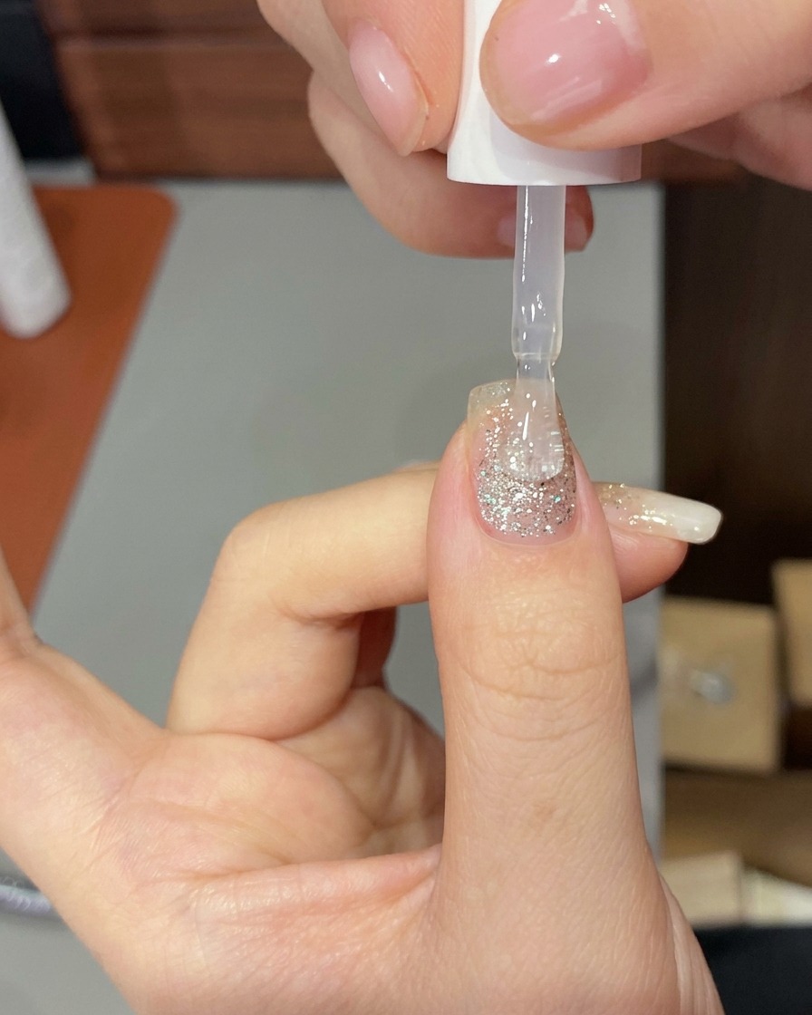 Eine Hand in einer professionellen UV/LED-Lampe, deren Nägel vom Härtungslicht beleuchtet werden.
