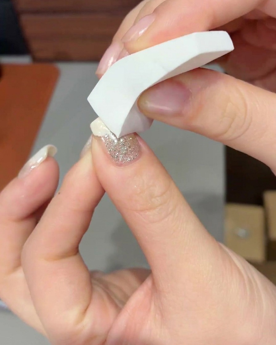 Nahaufnahme eines Make-up-Schwamms, der milchig-weißes Gel auf die Nagelspitze tupft, um einen sanften Verlauf zu bilden.