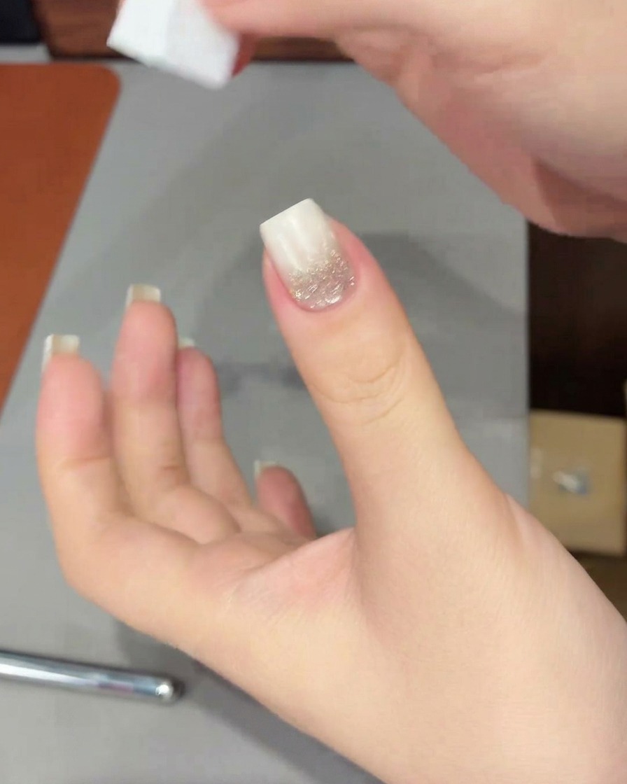 Eine Hand mit einem weißen Nagelverlauf wird in eine UV/LED-Lampe gelegt, um das frisch aufgetragene Gel auszuhärten.