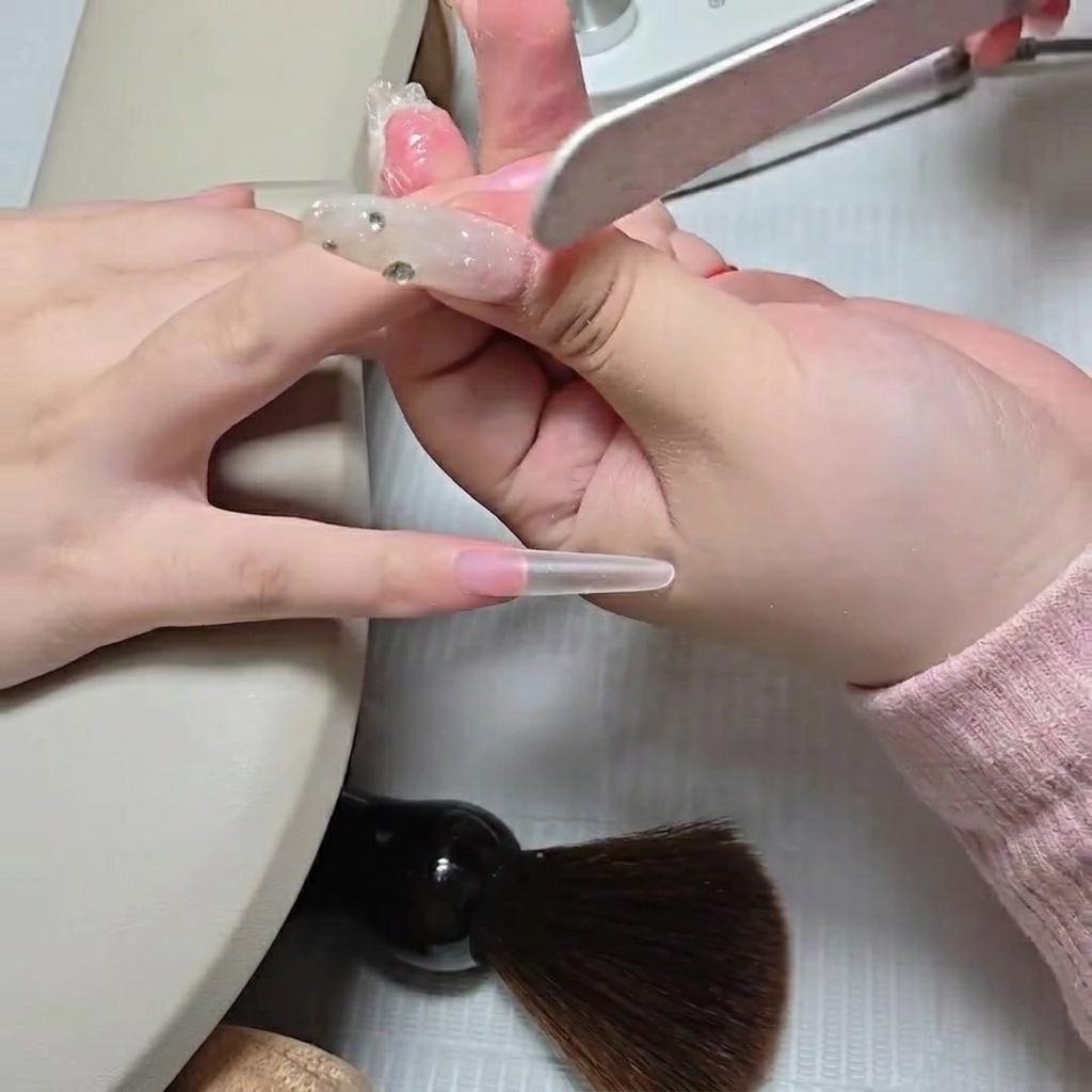 Eine Nagelfeile glättet den Übergang eines neu angebrachten Stiletto-Nageltipps am Naturnagel.