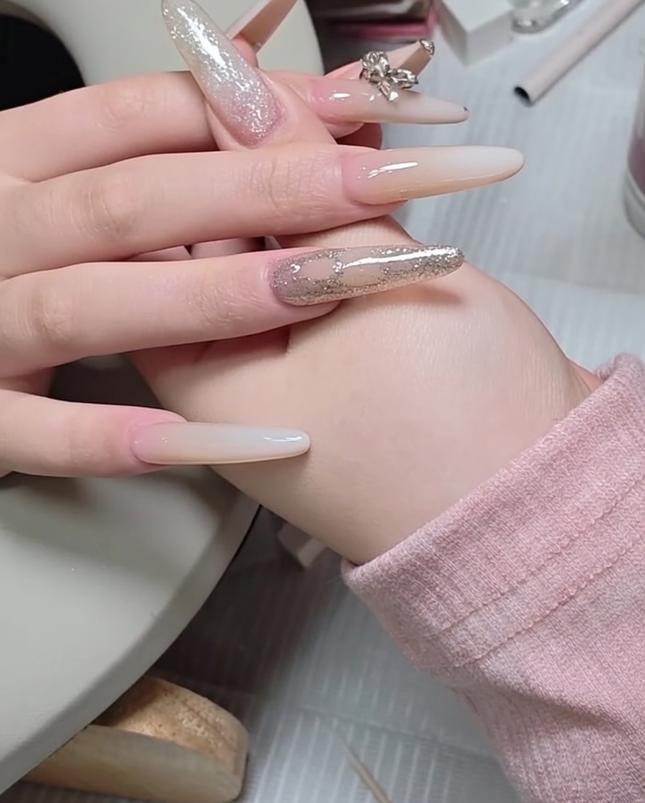 Ein Nagelhautschieber aus Metall wird genutzt, um einen kleinen Strassstein auf der Oberfläche eines manikürten Nagels auszurichten.