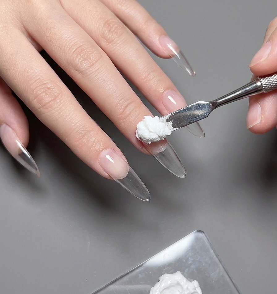 Nahaufnahme eines feinen Pinsels, der vorsichtig farbiges Gel aufträgt, um eine Herzschablone auf dem Daumen auszufüllen.