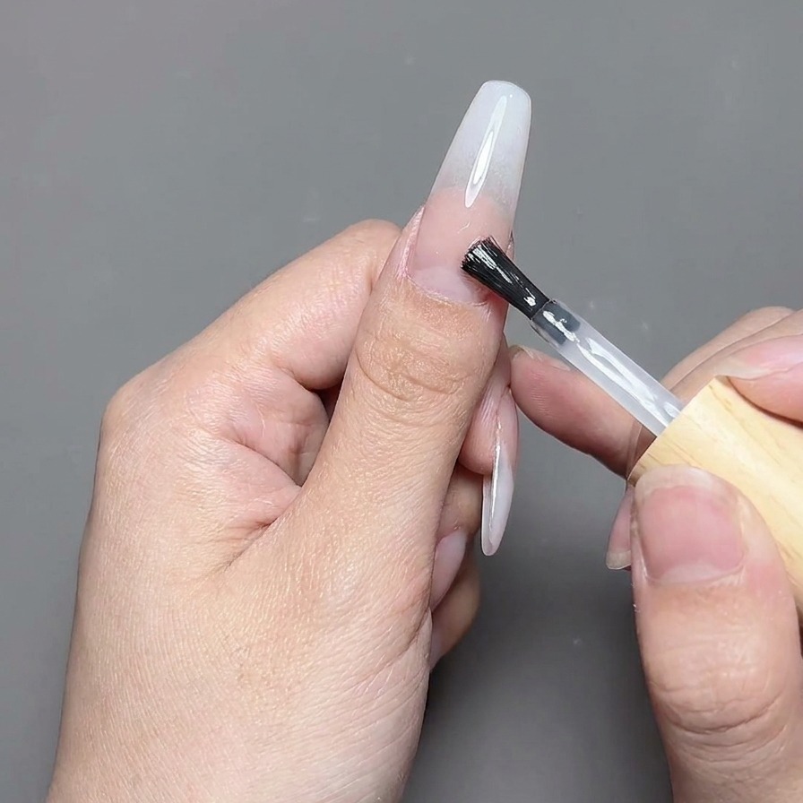 Ein Pinsel trägt einen klaren, glänzenden Top Coat über ein fertiges Nageldesign auf.