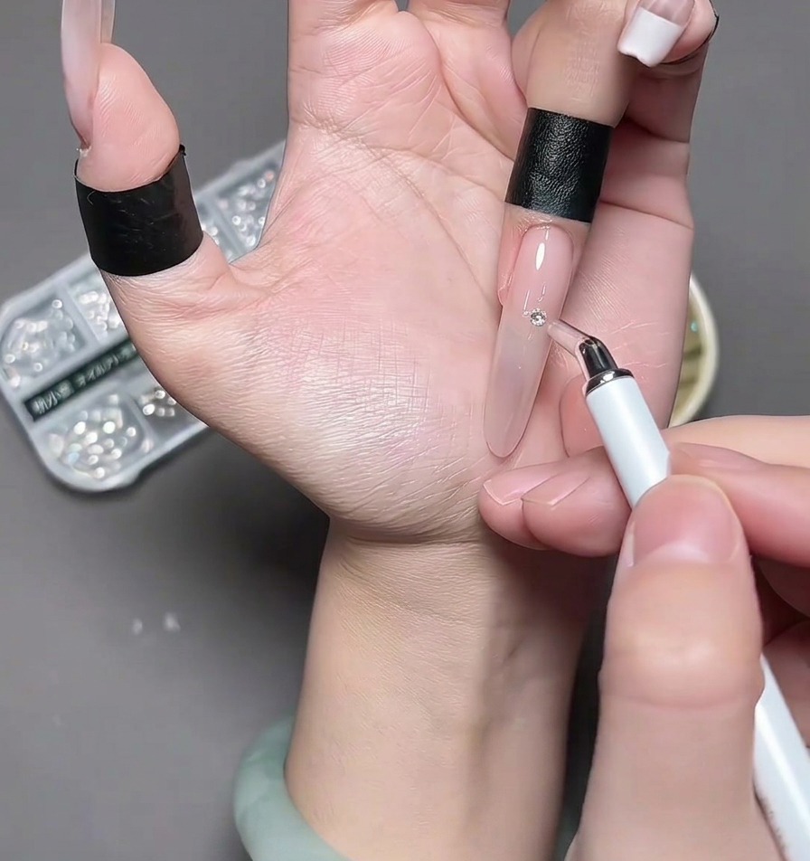 Eine Pinzette platziert ein kleines, silbernes Chrome-Herz in die Mitte eines Fingernagels.