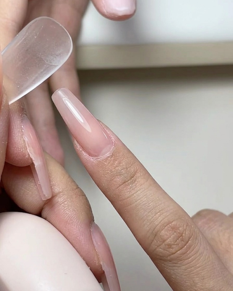 Ein Pinsel trägt eine glatte, klare Schicht Gel-Base-Coat auf einen Naturnagel auf.