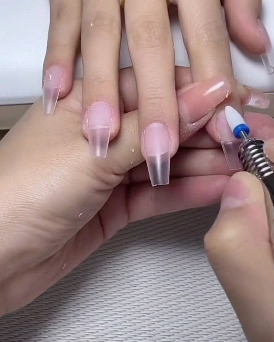Eine Nagelfeile poliert leicht die Oberfläche eines ausgehärteten Gel-Base-Coats auf dem Nagel.