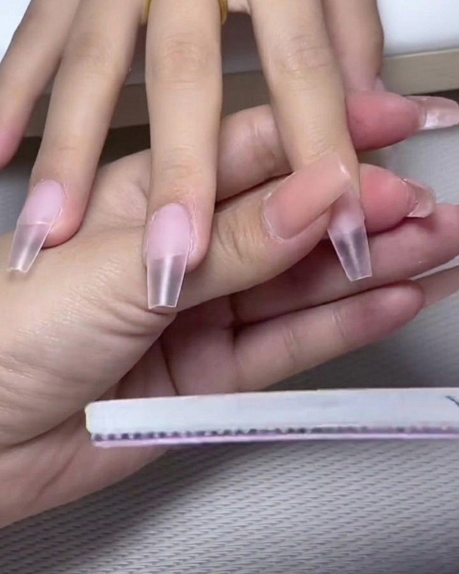 Ein Nagelpinsel trägt eine Schicht opakes milchweißes Gel auf die vordere Hälfte des Nagels auf.
