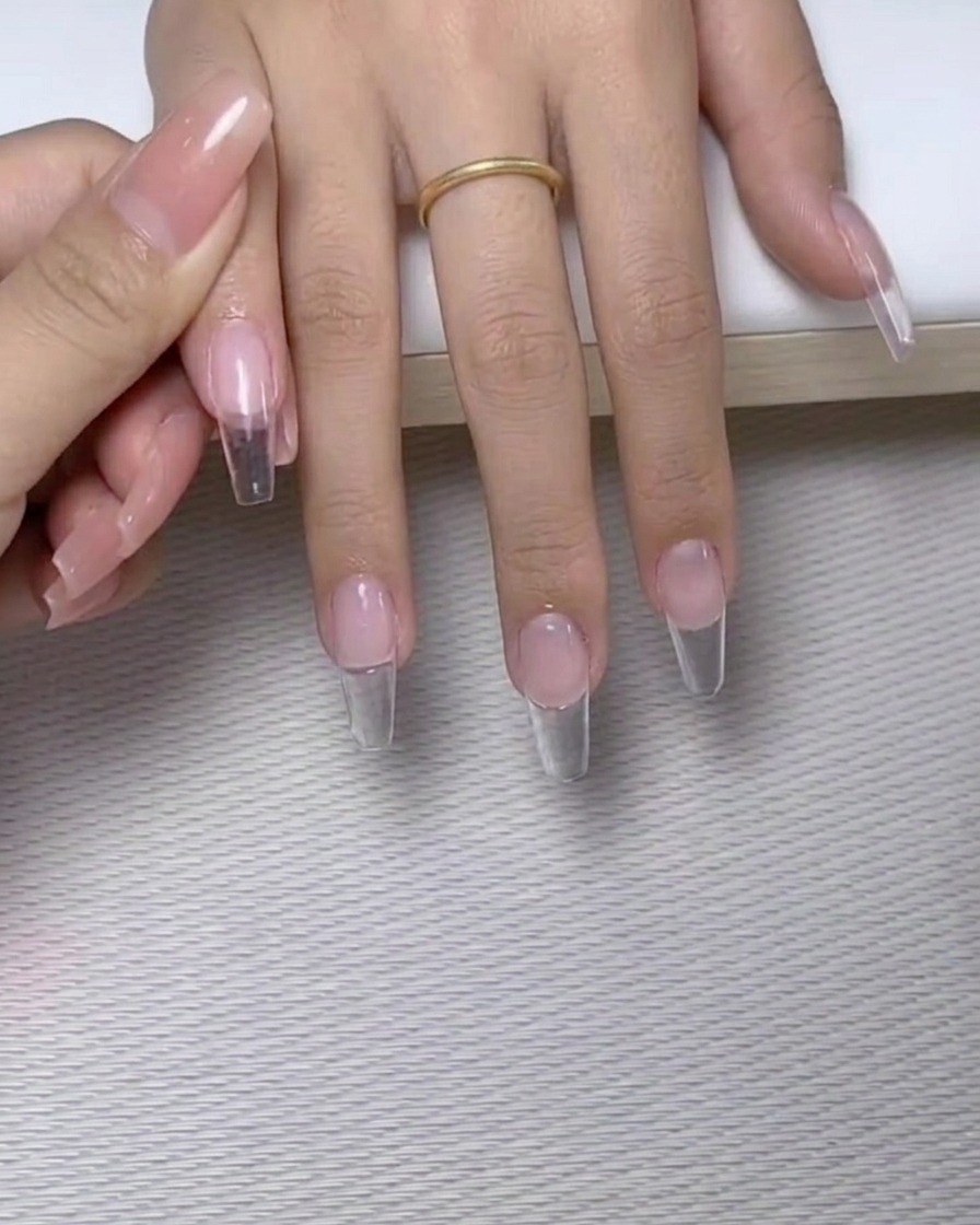Ein Pinsel mit feiner Spitze setzt kleine Punkte aus klarem Nagelkleber auf die Oberfläche eines manikierten Nagels.