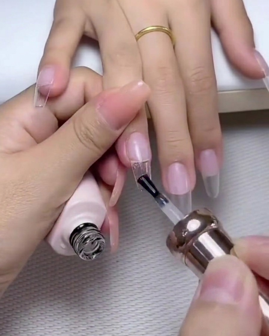 Ein Pinsel trägt eine Schicht glänzendes Top-Gel über einen Nagel auf, der mit Perlen und Strass verziert ist.
