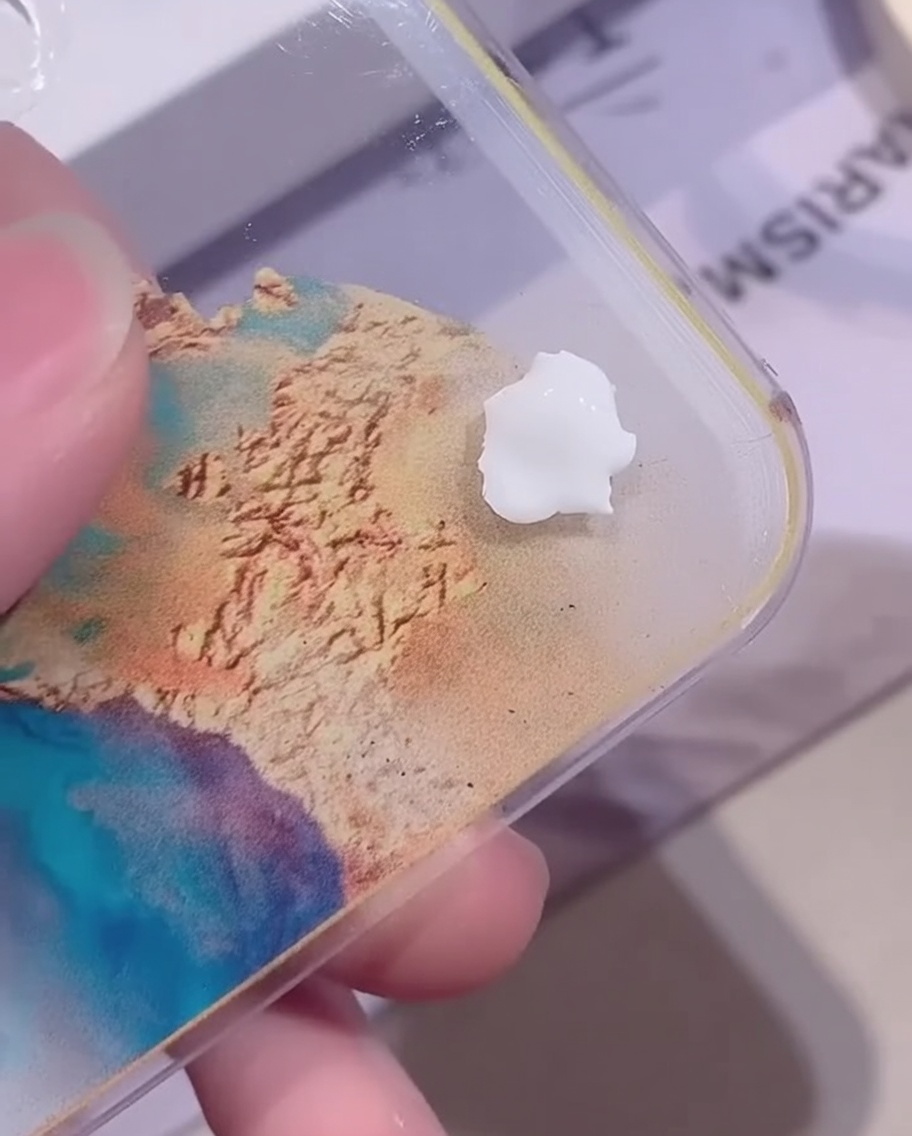 Ein kleiner Klecks opakes, weißes Farbgel auf einer klaren Acryl-Mischpalette vor einem farbenfrohen Hintergrund.