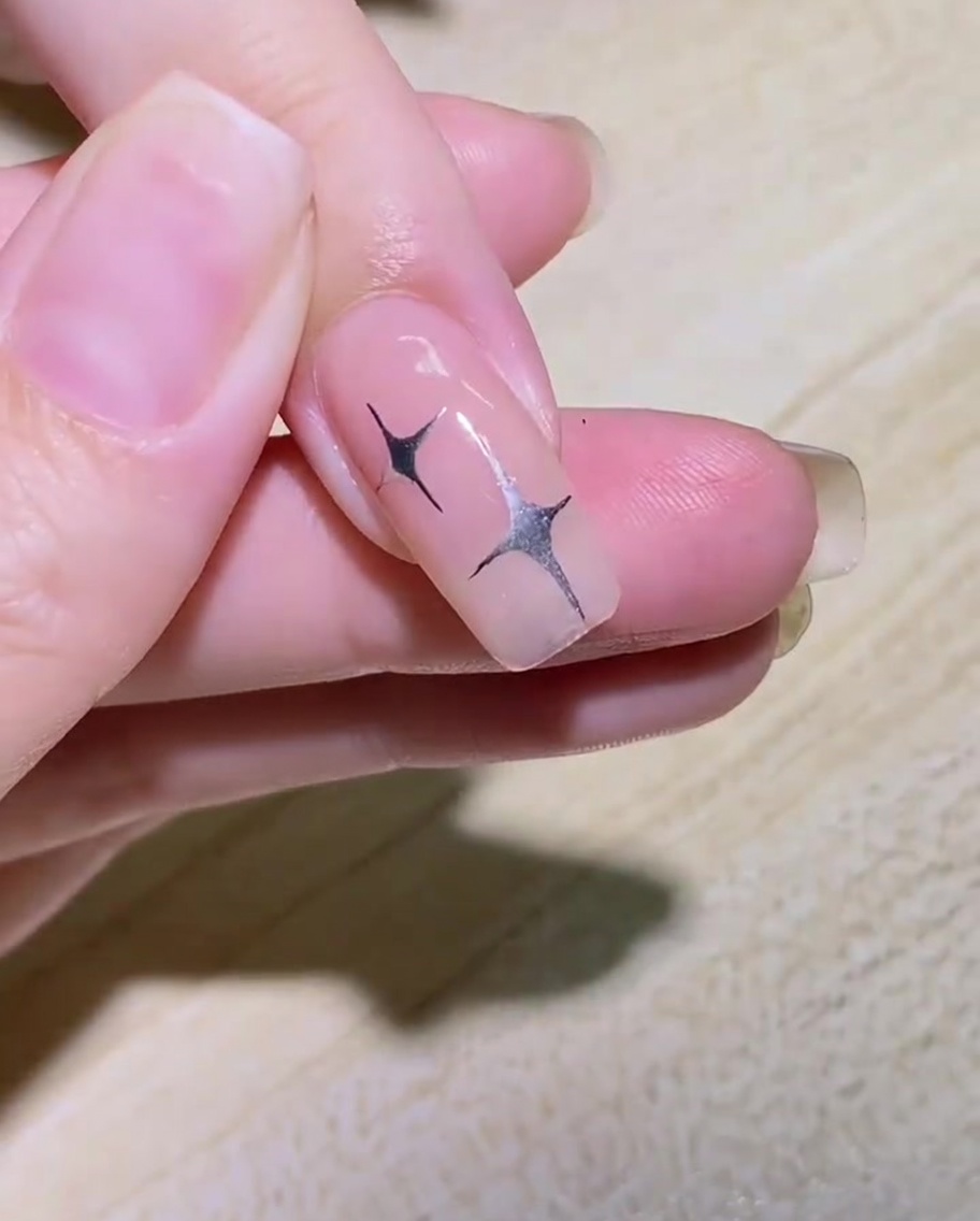 Ein Liner-Pinsel zeichnet den geschwungenen Umriss eines Schmetterlingsflügels auf die Seite eines Nagels.