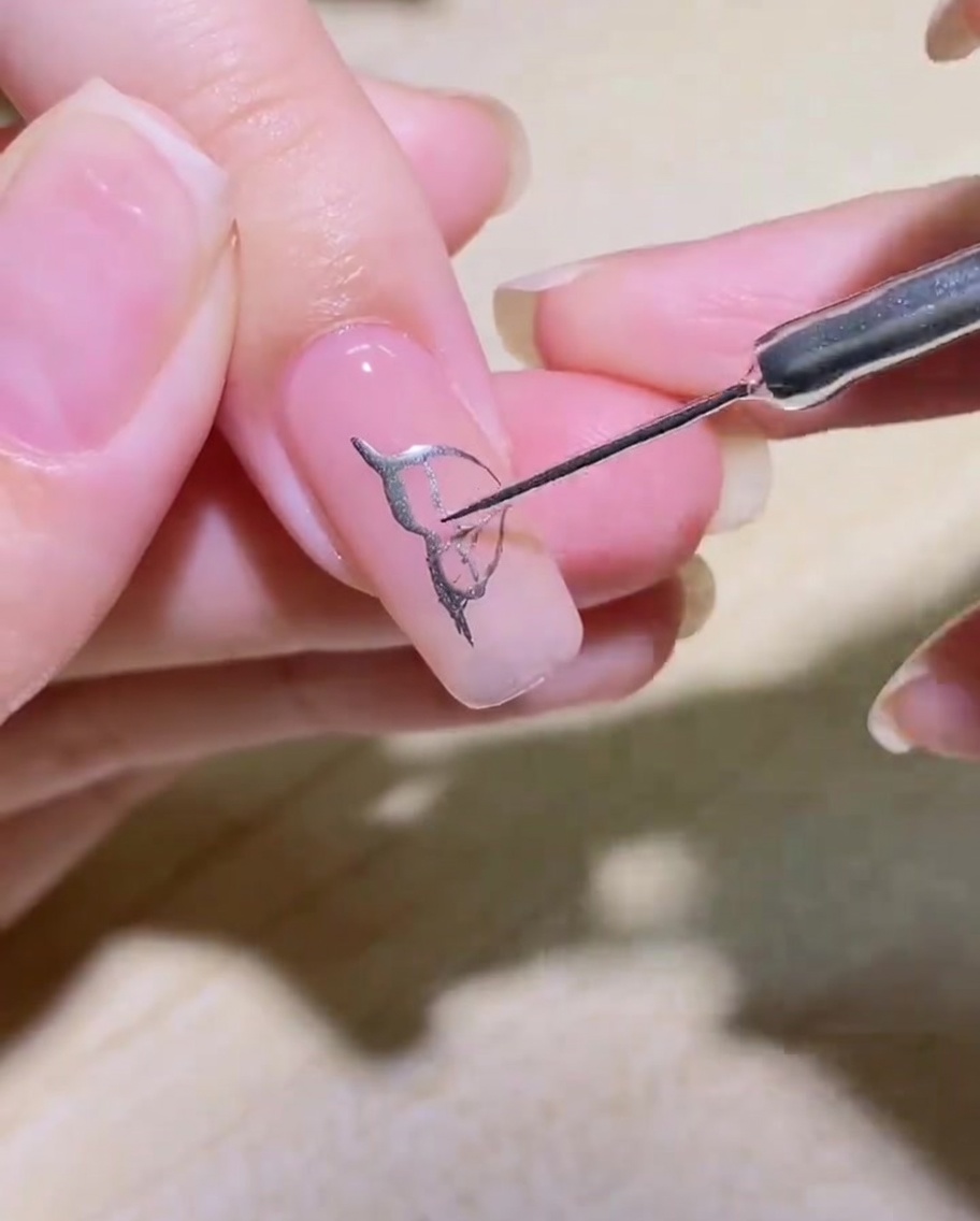 Nahaufnahme eines silbernen Schmetterlingsflügel-Designs mit feinen inneren Details auf einem Nagel.