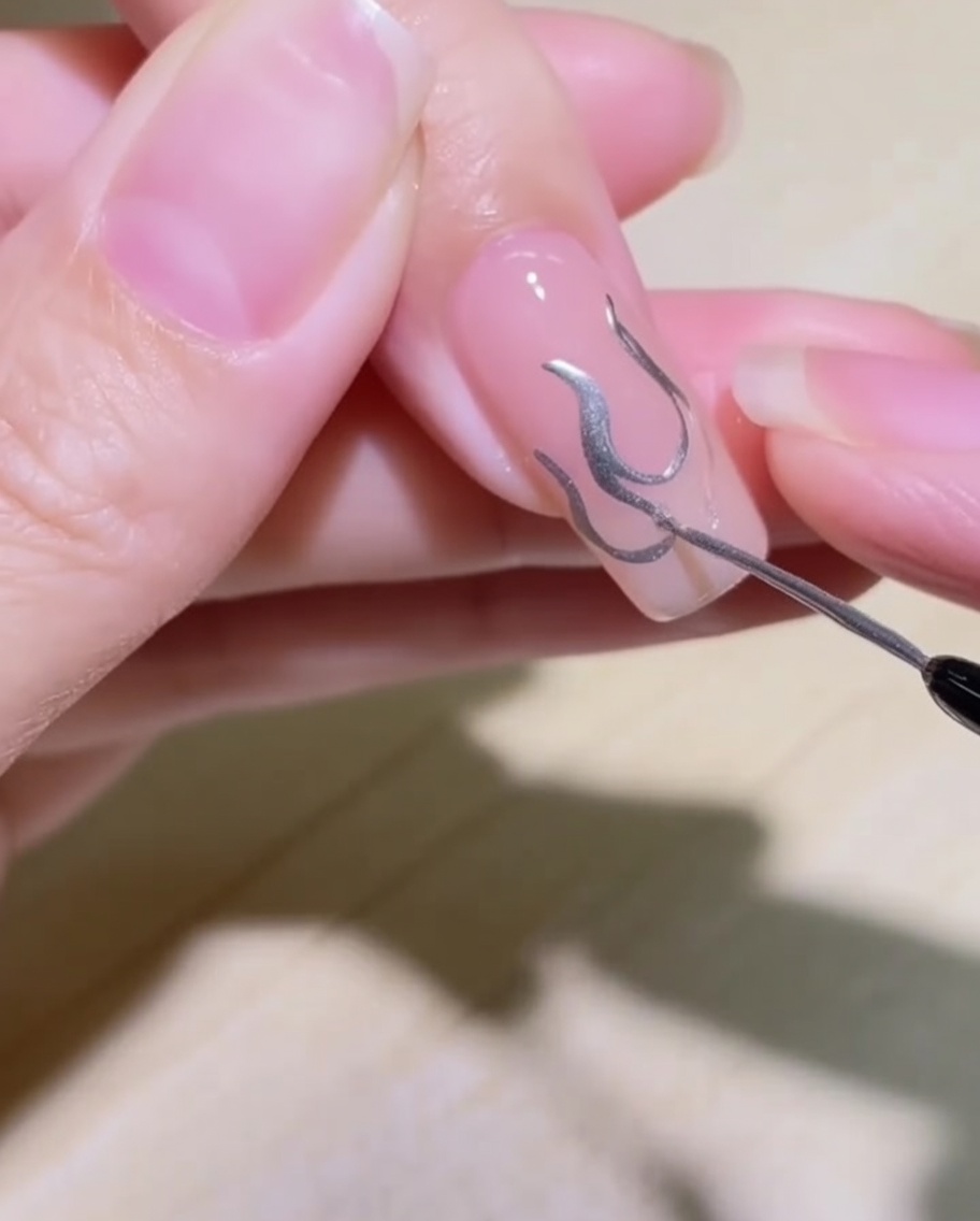 Nahaufnahme, die zeigt, wie das Flammendesign auf dem Nagel mit silbernem Metallic-Gel ausgefüllt wird.
