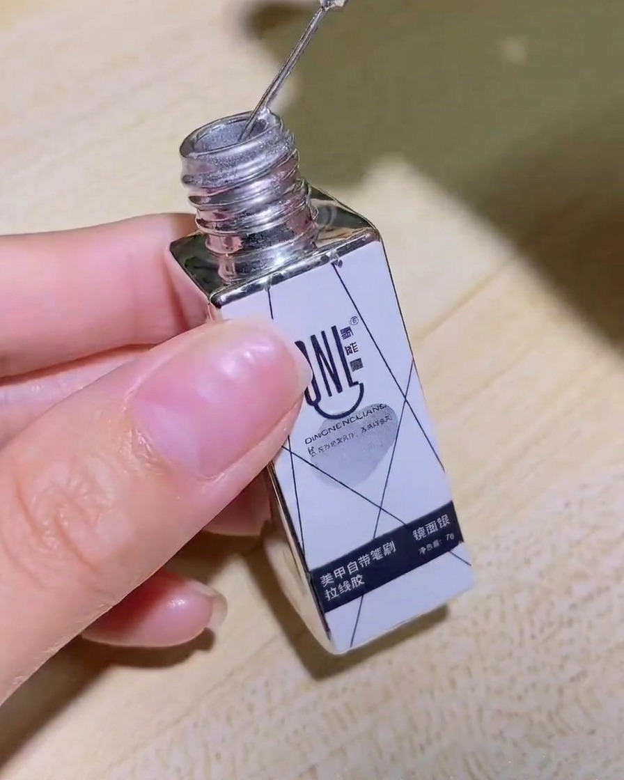 Eine Hand hält das Fläschchen mit silbernem Mirror-Liner-Gel, das Produktetikett ist deutlich sichtbar.