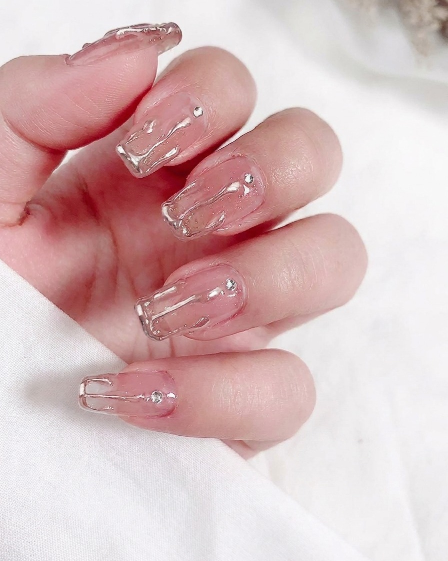 Nahaufnahme eines Pinsels beim Auftragen einer Schicht transparenten Nude-Gellacks auf einen Naturnagel.