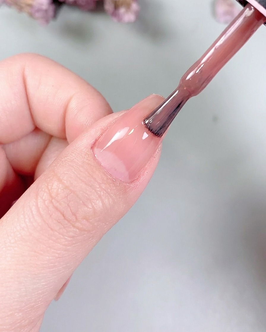 Ein kleiner flacher Gelpinsel, der die Nude-Farbe sanft auf der Nageloberfläche glättet.