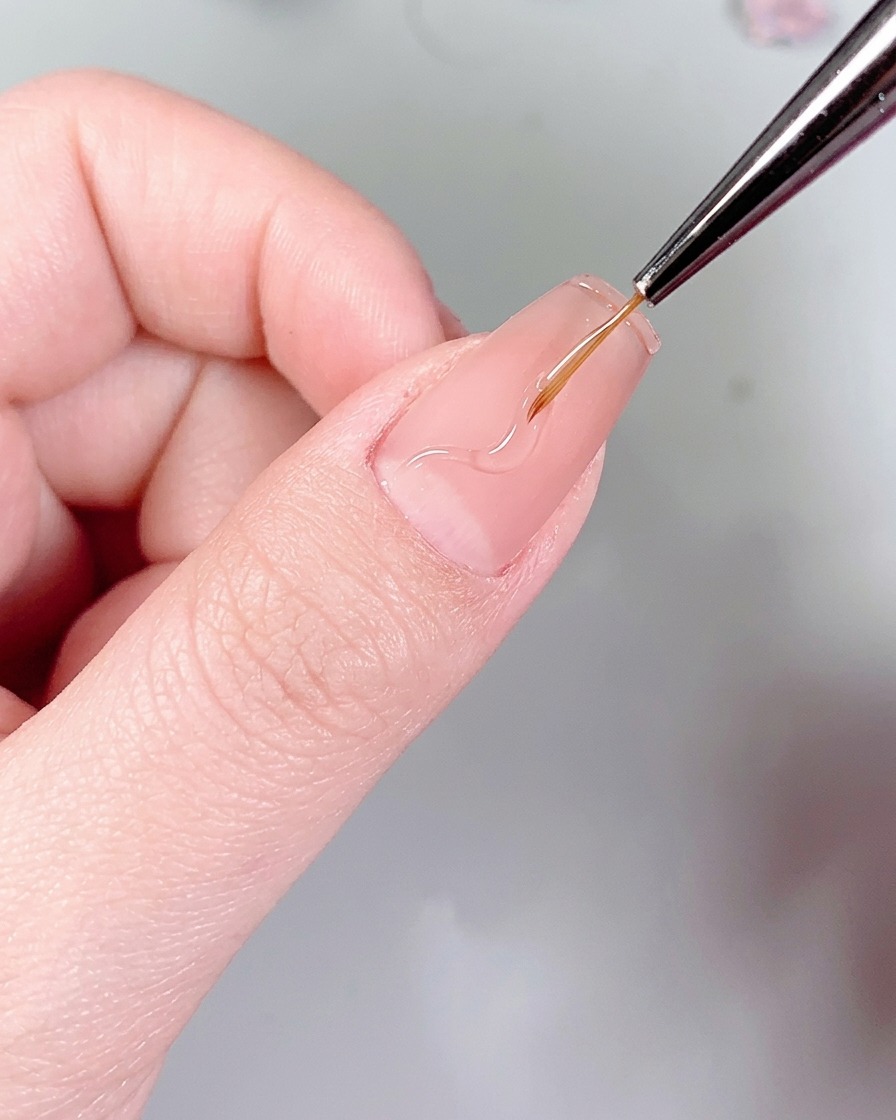 Ein feiner Liner-Pinsel zeichnet zarte, wellige Flammenmuster mit klarem Nagelkleber auf einen Nagel.