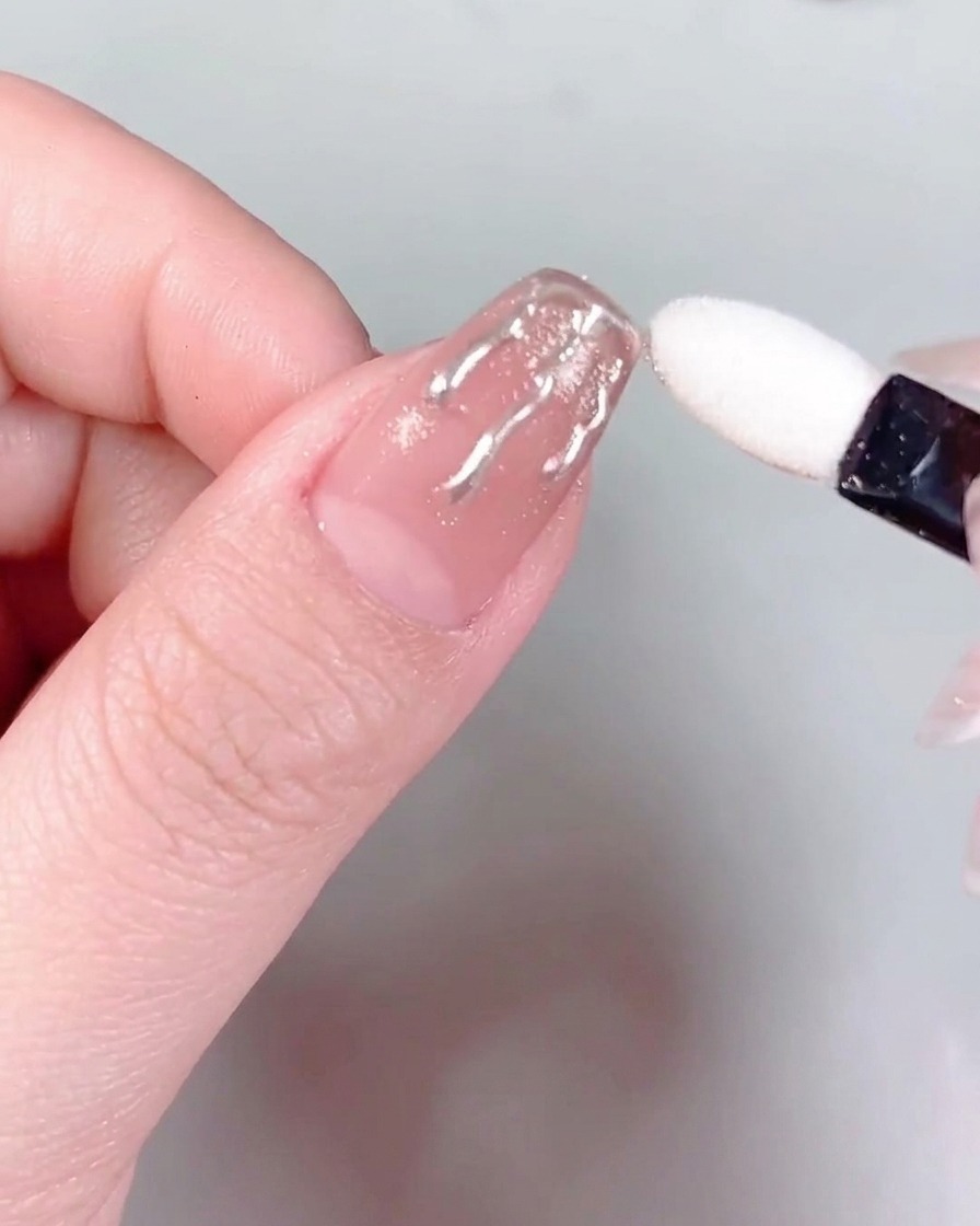 Eine Pinzette hält einen kleinen, funkelnden Strassstein und positioniert ihn an der Basis eines manikierten Fingernagels.