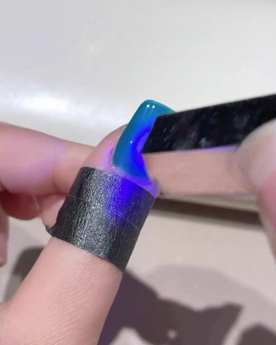 Eine kleine handgeführte UV-Lampe leuchtet blaues Licht über einen tiefblauen Cat-Eye-Gelnagel, um das Design auszuhärten.
