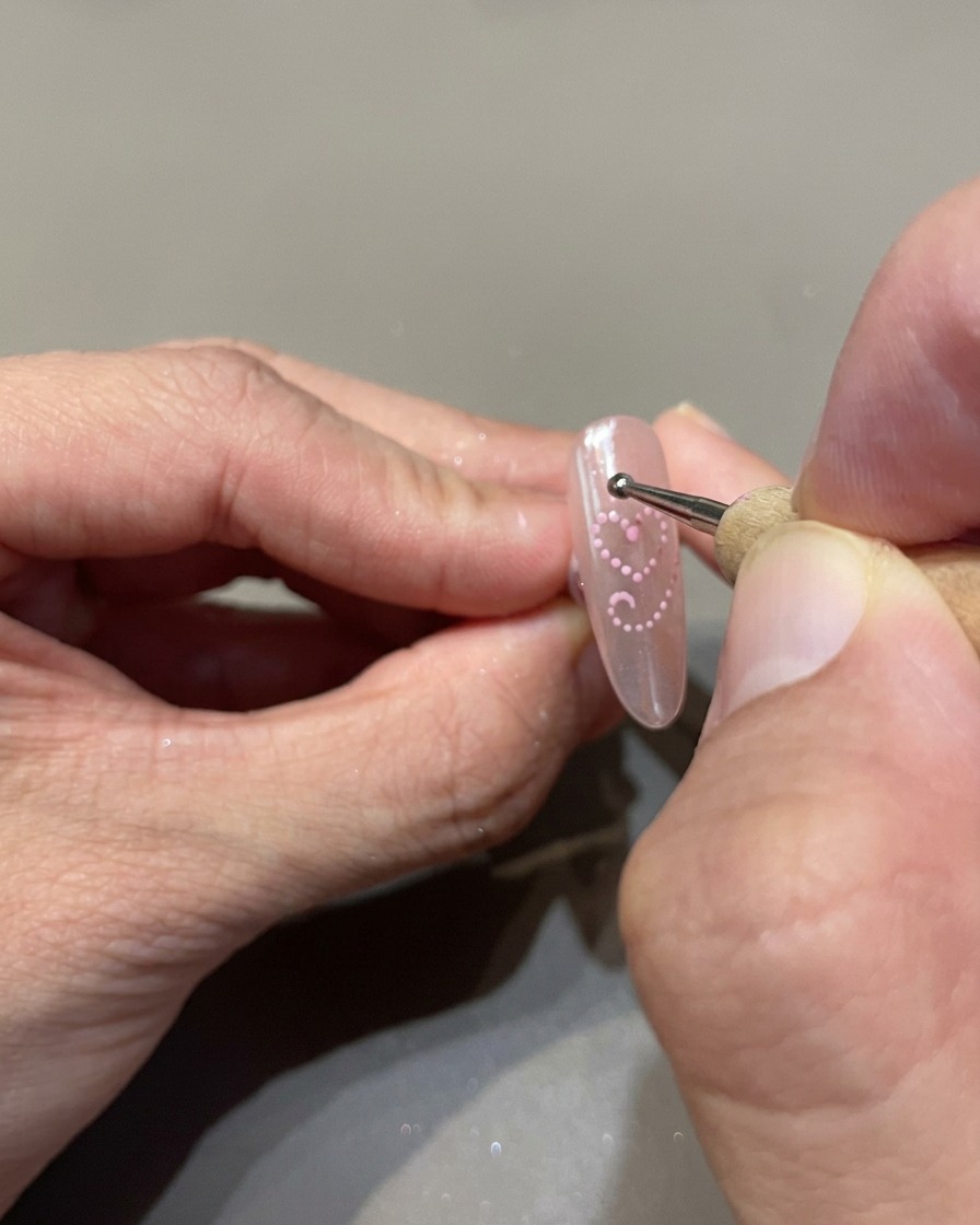 Ein Dotting-Tool platziert kleine, gleichmäßige Punkte aus rosa Cat-Eye-Gel als Herzform auf dem Nagel.