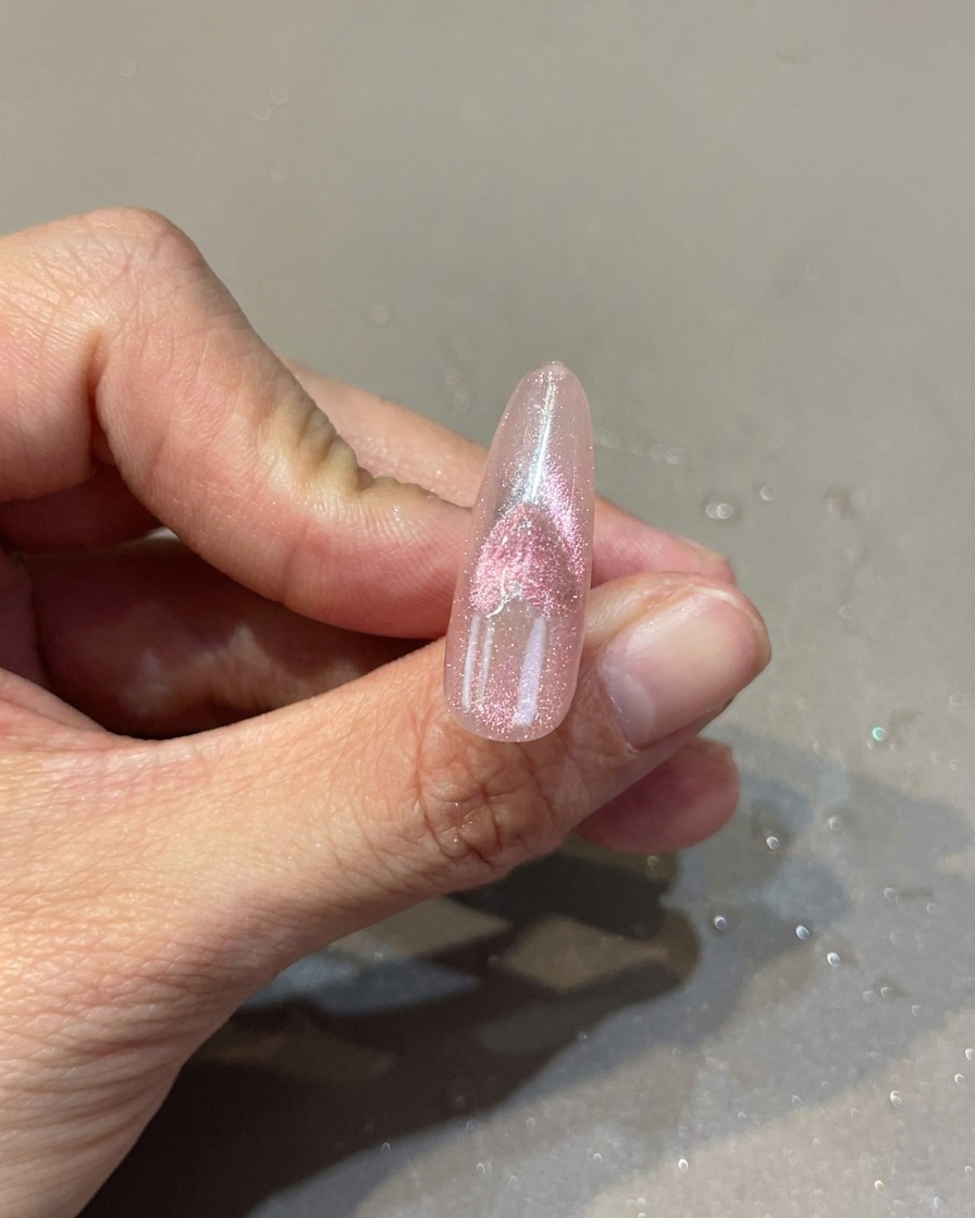 Ein rosa Nagel mit Herz-Cat-Eye-Design, während ein Magnet den Schimmer manipuliert.