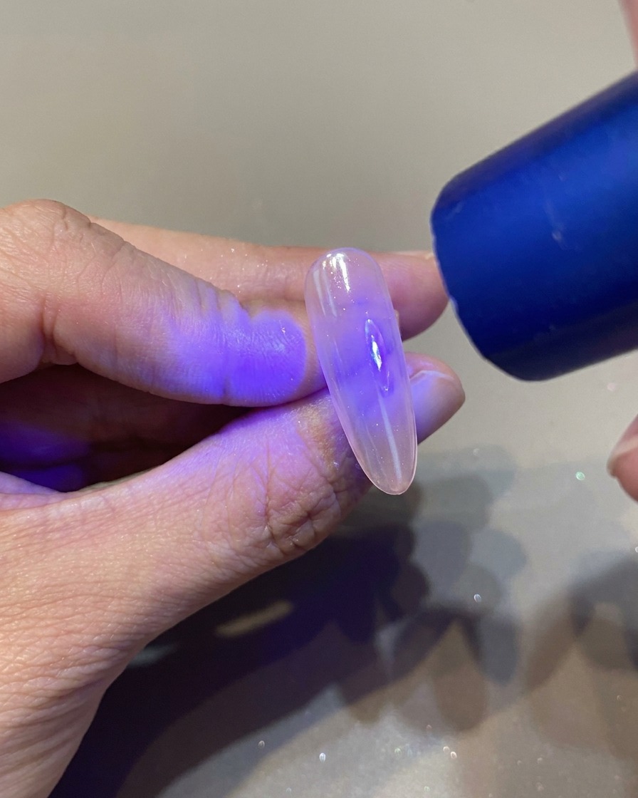 Ein Nagelpinsel trägt einen klaren, glänzenden Top Coat auf einen manikürten Nagel auf.