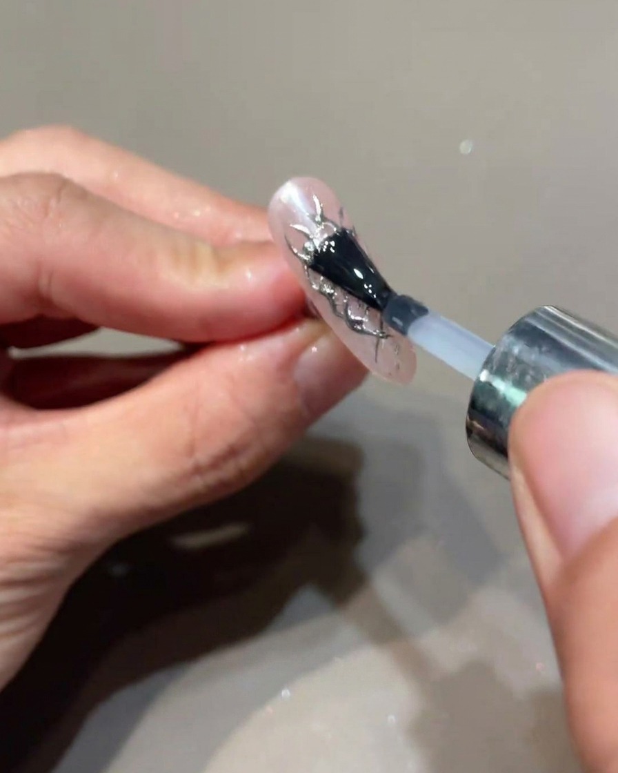 Ein Pinsel trägt eine finale Schicht Top Coat über die verzierten Nägel auf.