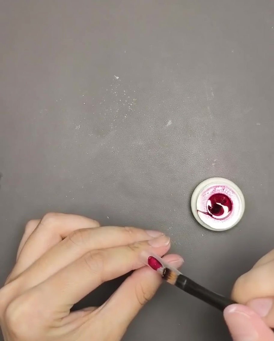 Nahaufnahme eines Pinsels, der tiefrotes Cat-Eye-Gel auf eine Nagelspitze aufträgt.
