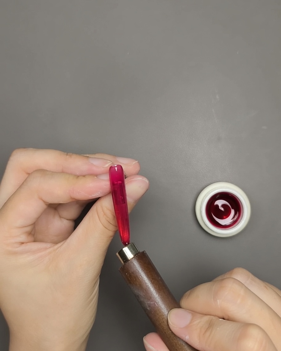 Eine Hand hält einen Stabmagneten nah an einen Nagel mit rotem Cat-Eye-Gel, um den Schimmer zu aktivieren.
